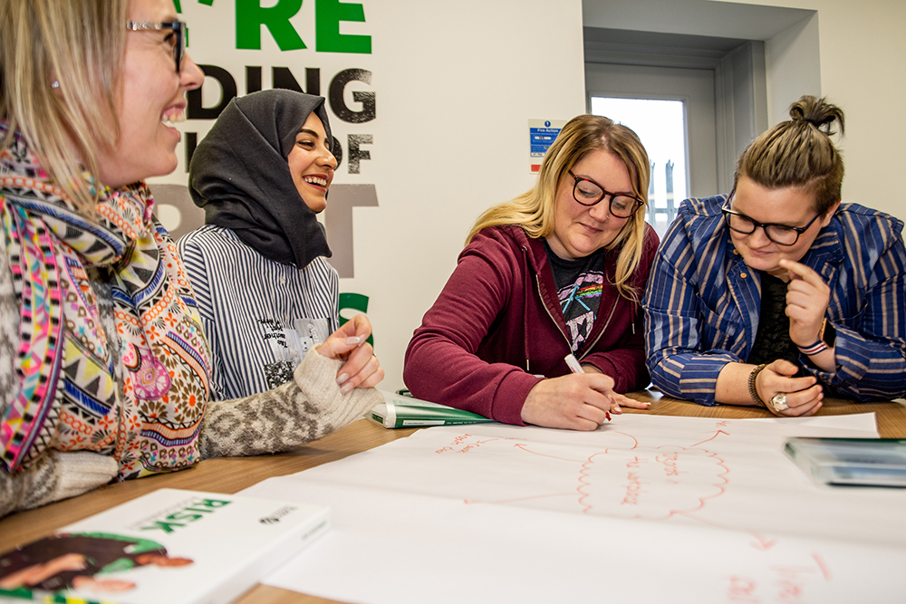 Course attendees work together on a group exercise around a table, making notes on a large sheet of paper