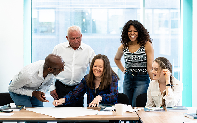 Employees gathered around a desk, all are smiling.